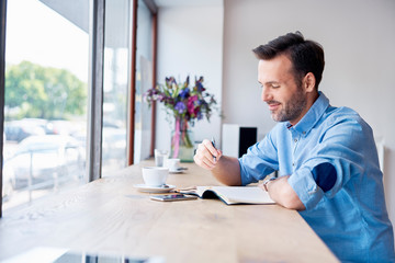 Man sitting in cafe drinking coffee and writing in personal calendar