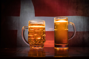 Creative concept. Beer glasses on table at dark toned foggy background with blurred view of flag of Denmark. Support your country with beer concept.