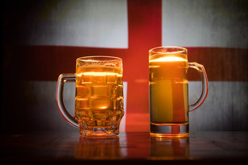 Creative concept. Beer glasses on table at dark toned foggy background with blurred view of flag of England. Support your country with beer concept.