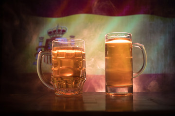 Creative concept. Beer glasses on table at dark toned foggy background with blurred view of flag of Spain. Support your country with beer concept