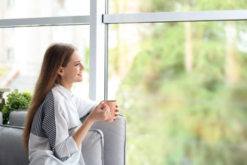 Young beautiful woman drinking morning coffee near window at home