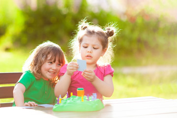 Two adorable little girls playing board game outdoors