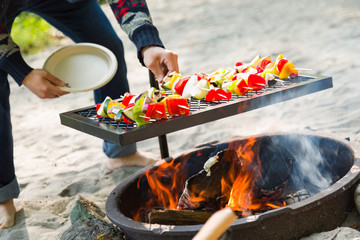 Young Adult Mixed Race Man Placing Vegetable Kaboobs Onto Outdoor Grill