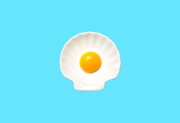 Egg yolk on white shell plate on blue background. Top view. Minimalistic design, colorful background