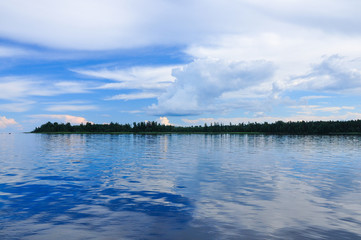 Blue sky with Cumulus clouds over the forest at the Lake Ladoga shore