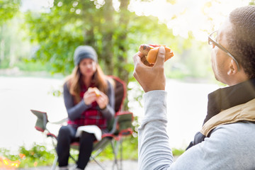 Obraz premium African American Man Enjoying Hot Dog with Friends at Campground