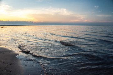 Naklejka premium Sea waves on the sandy beach in sunset. Ladoga lake