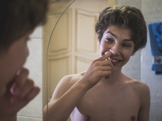 young naked male teenager picking his nose in front of mirror in bathroom