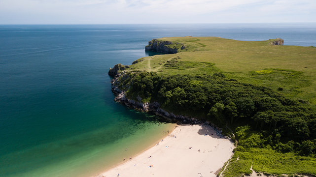 Aerial drone view of a beautiful sandy beach inside a bay surrounded by cliffs and farmland (Barafundle Bay, Wales)
