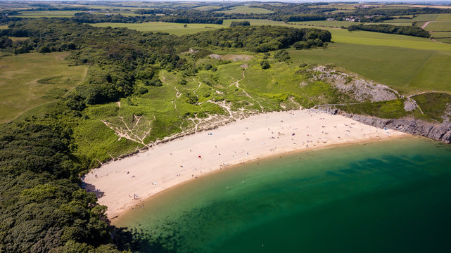 Aerial drone view of a beautiful sandy beach inside a bay surrounded by cliffs and farmland (Barafundle Bay, Wales)