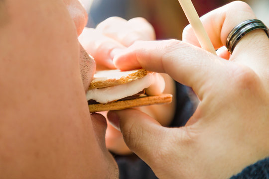 Closeup Of Man Earing Smore With Roasted Marshmallow And Chocolate At Campfire Outdoors