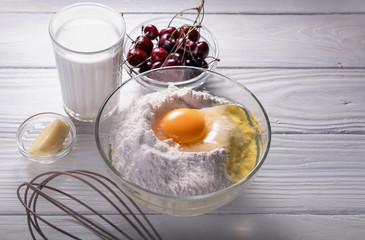 Cherry pie preparation process. Close up ingredients - milk, butter, egg, flour, cherry on a white wooden background.Food background