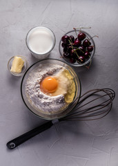 Cherry pie preparation on grey background. Ingredients - milk, butter, egg, flour, cherry. Food background. Vertical shot.