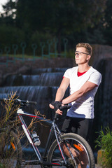 Healthy Lifestyle and Sport Concepts.Caucasian Male Athlete with Mountain Bike Posing Against Waterfall Outdoors.