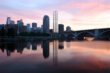 Fototapeta premium Urban city architecture background. Minneapolis downtown skyline and Third Avenue Bridge above Saint Anthony Falls and Mississippi river. Beautiful colors after sunset sky reflected in a water. 