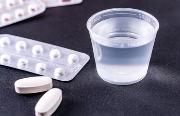 Tablets and plastic glass with water on a black background