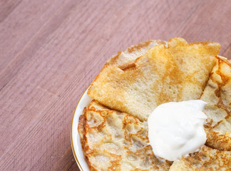 Plate with hot pancakes with sour cream on a wooden background