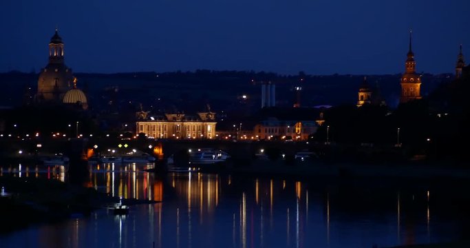 Night skyline in Dresden, with view over the historic buildings and their towers, Carola Bridge and ferry on Elbe River (Saxony, Germany)