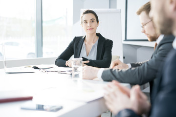 Group of young entrepreneurs sitting at meeting table in conference room and discussing startup projects, focus on smiling businesswoman listening to colleagues, copy space
