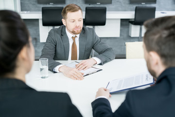 Portrait of modern young businessman reading contract from partners while  sitting at meeting table in conference room, copy space