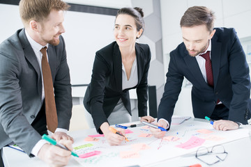 Portrait of three businesspeople with smiling young woman  standing at table in conference room  drawing charts while planning strategy, copy space