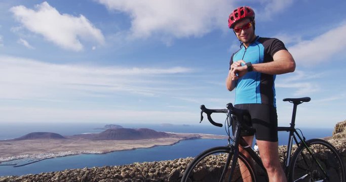 Cyclist biking looking at smartwatch while riding road bike. Cycling athlete biker using activity tracker gps fitness watch on biking workout. Sports man using his watch app for fitness tracking.