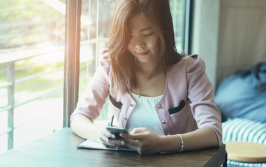 Obraz premium beautiful business lady in smart casual wear is holding a pencil,with mobile phone. and smiling while sitting at the desk in office