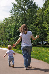 Fototapeta premium Family. Mom and son in city park. Girl and little boy are walking. Shooting from back. People are unrecognizable.
