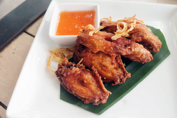 Fried chicken wings with sauce in white plate on wooden table..