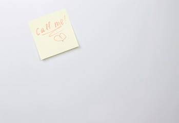 Yellow sticker paper sheet with words call me and painted heart on a white board.