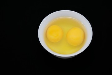 Top view of egg yolk and white in a bowl isolated on black background. Copy space