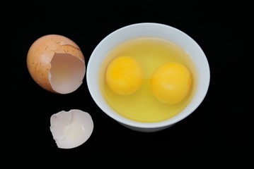 Top view of egg yolk in a bowl and egg shell isolated on black background. Copy space