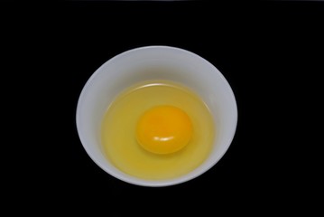 Top view of egg yolk and white in a bowl isolated on black background. Copy space