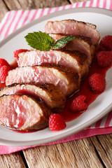 Sliced fried duck breast with fresh raspberry sauce and mint closeup on a plate. vertical