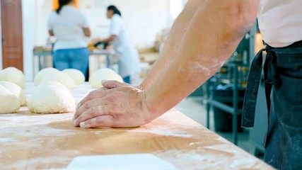 Fototapeta premium Professional baker is forming pieces of dough in bakery commercial kitchen.