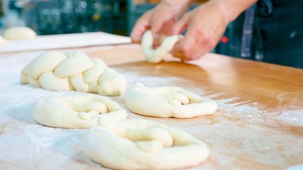 Professional baker is forming pieces of dough in bakery commercial kitchen.