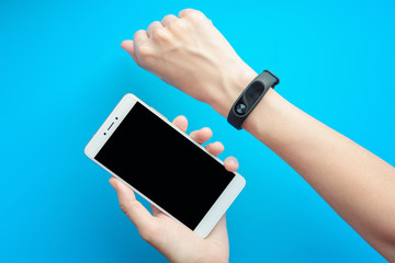 woman's hand with fitness tracker and smartphone on blue background