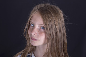Naklejka premium Beautiful blond young girl with freckles indoors on black background, closeup portrait