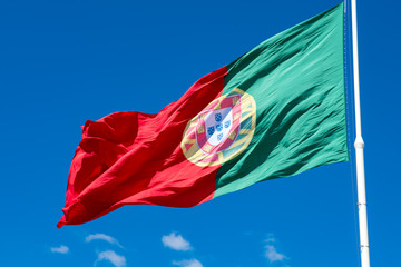 National flag of Portugal on a flagpole in front of blue sky.