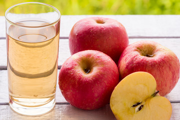 Glass of apple juice and red apples on wooden table with natural green background