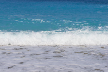 Foamy waves lapping on beach; The sea the colors of the sky or azure colour on the coast as natural background; The wave approaches the shore