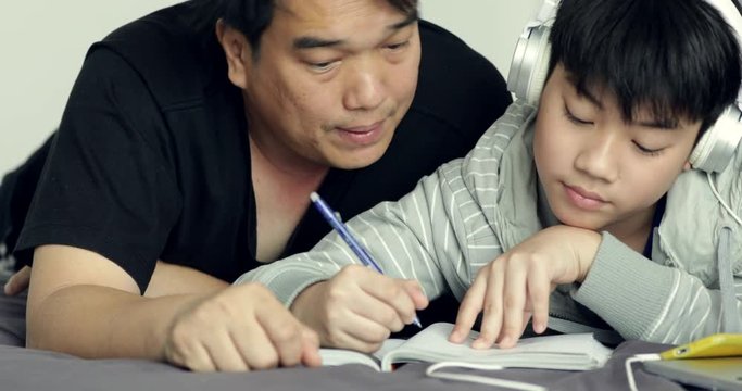 Asian father helps his young son while the boy is doing his homework at home
