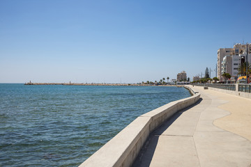 Cyprus, Larnaca city. Stone path around and above the sea. Port, beach, buildings, blue sky backdrop.