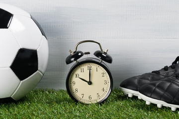 ball and leather boots for playing football next to the clock on a green background of grass