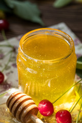 Open glass jar of liquid honey and honey dipper, bunch of linden flowers