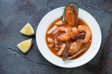 French seafood soup or buyabes in a white plate, cracked asphalt background, high angle view, studio shot