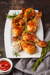 Grilled spicy chicken legs baked with garlic, rosemary and thyme on dark background.