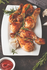Grilled spicy chicken legs baked with garlic, rosemary and thyme on dark background.