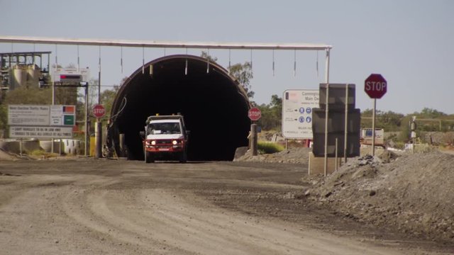 A small white and orange colored truck comes out of a construction tunnel.