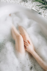 Nude legs of female person lying in bath with foam